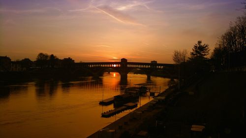 Silhouette bridge over river against sky during sunset