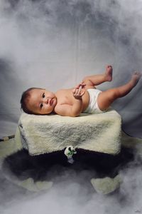 Portrait of baby girl lying on bed amidst smoke