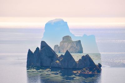 Double exposure of rocks in sea against sky during sunset