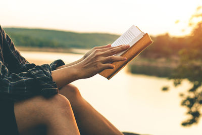 Midsection of woman with umbrella sitting against sky during sunset