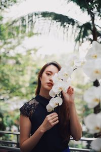 Portrait of beautiful young woman holding flowering plant