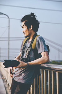 Side view of young woman using phone while standing on railing