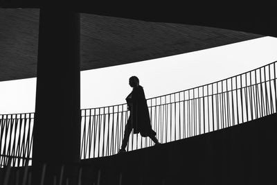 Silhouette man walking on bridge against clear sky