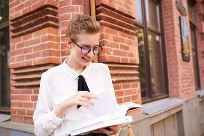 Beautiful young woman reading book against brick wall