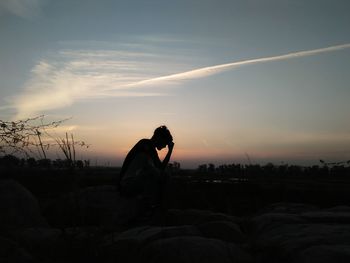 Silhouette of man sitting against sky during sunset