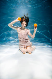 Full length of woman holding oranges under water