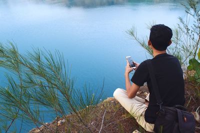 High angle view of man using mobile phone while sitting on cliff