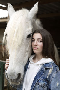 Portrait of teenage girl with horse standing at stable