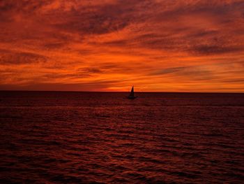 Silhouette sailboat sailing on sea against orange sky