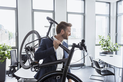 Smiling businessman with bicycle on his shoulder in the office