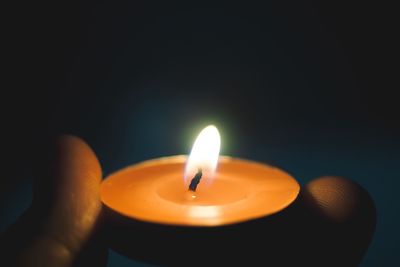 Close-up of hand holding lit candle at night