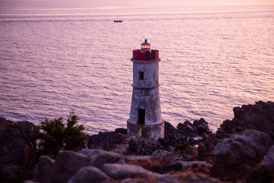 Lighthouse on rock by sea against sky