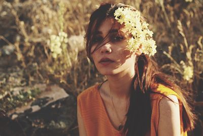 Portrait of young woman wearing flowers while sitting on field during sunset