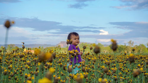 Cute girl standing amidst yellow flowering plants