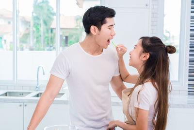 Girlfriend feeding boyfriend while standing in kitchen