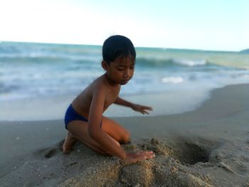 Side view of shirtless boy playing with sand at beach