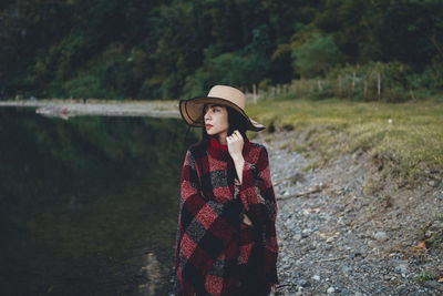 Woman wearing hat standing against trees