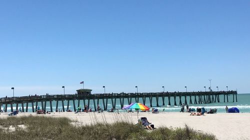 People at beach and a fishing pier against clear blue sky