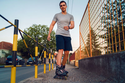 Full length of young man standing with roller skates on footpath
