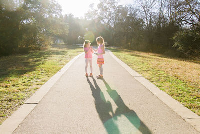 Full length of siblings standing on footpath in park against trees