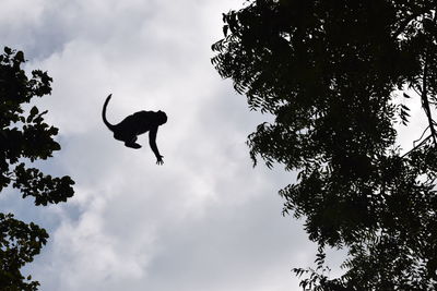 Low angle view of silhouette man jumping against sky