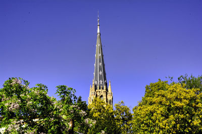 Low angle view of trees and building against clear blue sky