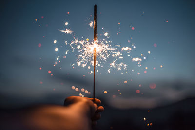 Cropped hand holding sparkler at night