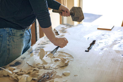 Midsection of male carpenter chiseling wood in workshop