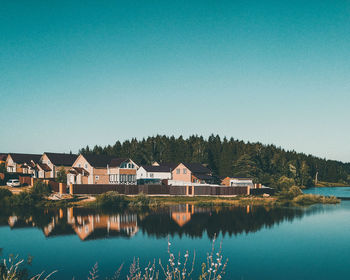 Houses by lake against clear blue sky