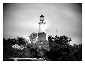 Lighthouse by trees against sky