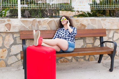 Young woman sitting on bench against brick wall