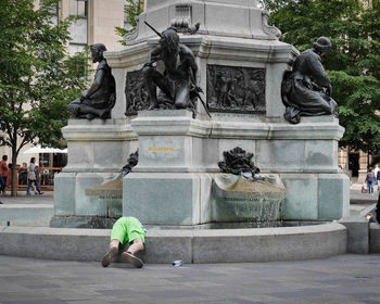 Rear view of young boy bent over and playing in a public water fountain.