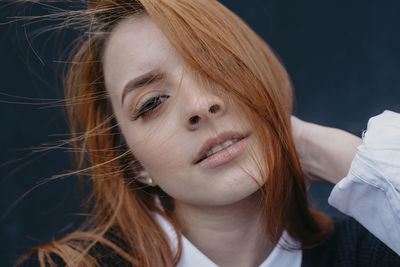 Young content redhead female with wind in hair standing in city and looking at camera