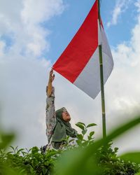 Low angle view of woman holding flag against sky