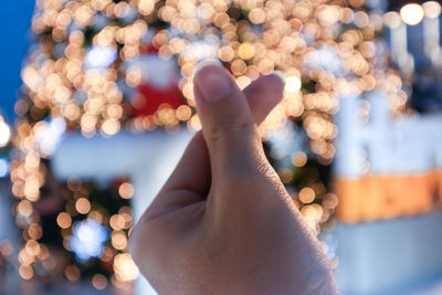 Cropped hand gesturing against illuminated christmas tree