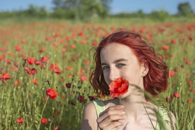 Portrait of young woman standing amidst flowering plants on field