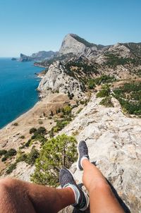 Low section of person on sea shore against mountains