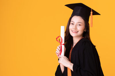 Portrait of smiling young woman against yellow background