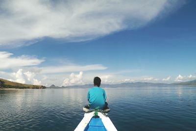 Rear view of man sitting on boat in lake against sky