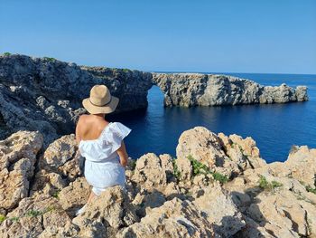 Rear view of woman sitting on rock against clear sky