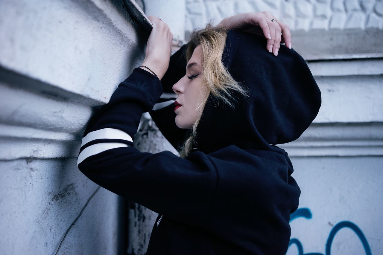 real people, one person, lifestyles, architecture, women, wall - building feature, clothing, day, leisure activity, young adult, young women, built structure, adult, casual clothing, black color, standing, side view, three quarter length, outdoors, hairstyle, warm clothing