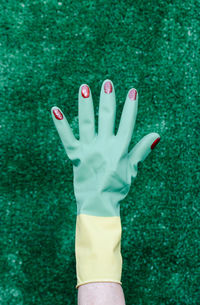 Hand with plastic glove and nails painted red on a green background