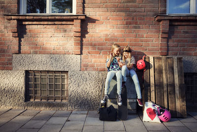 Full length of girls sitting against building in city