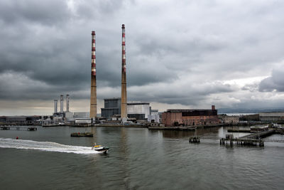 View of city at waterfront against cloudy sky