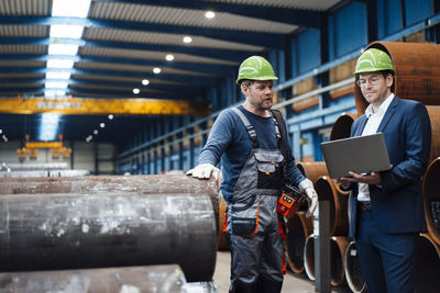 Male manager using laptop while standing by warehouse worker in factory