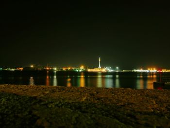 Illuminated city by sea against clear sky at night