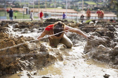 Woman crossing dirty field under barbed wires during race