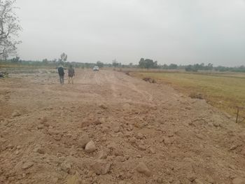 Rear view of people walking on field against sky