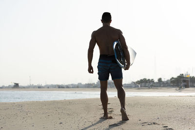 Rear view of man standing on beach against clear sky