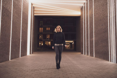 Full length of woman walking against illuminated lights on wall